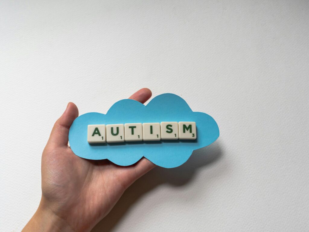 Close-up of hand holding scrabble tiles spelling 'autism' on a blue cloud cutout, emphasizing awareness.